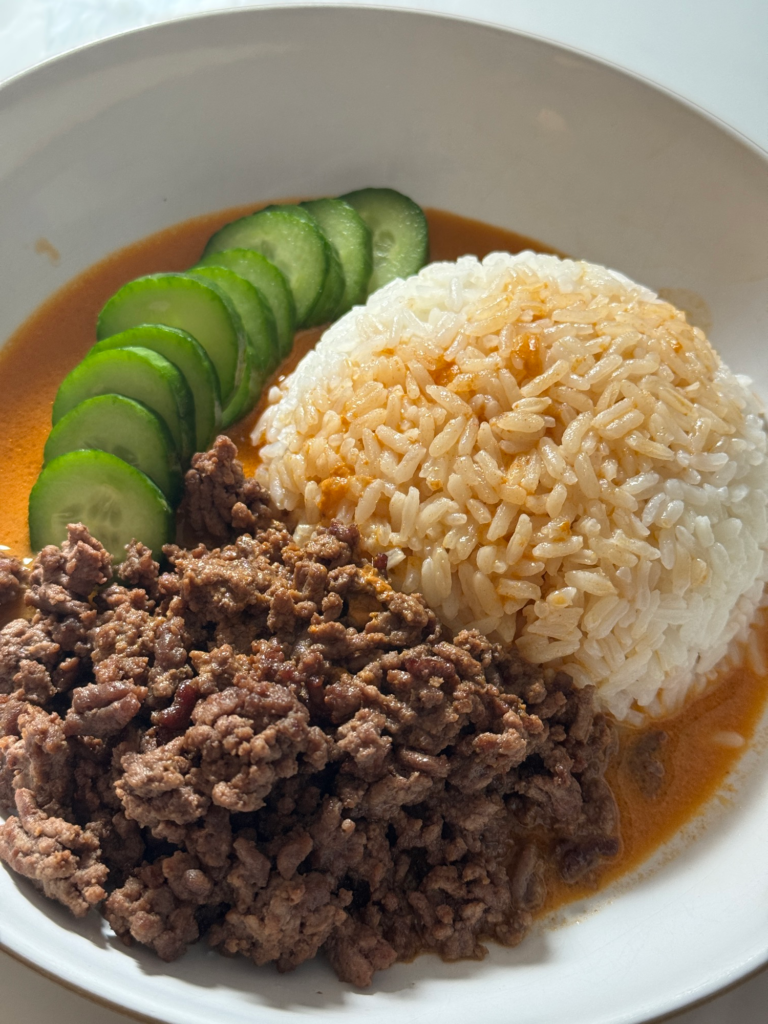 An assembled brothy beef bowl with rice, cucumber, ground beef, and broth