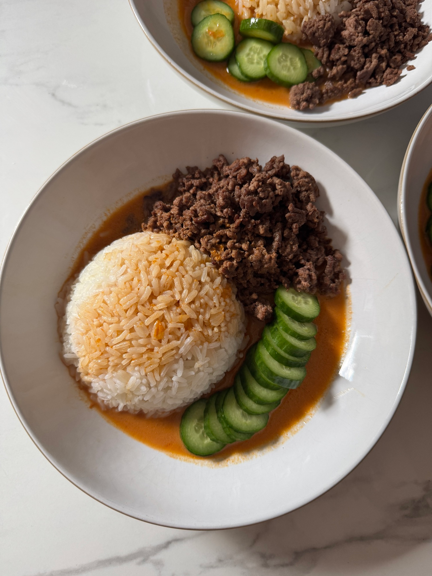 A brothy beef bowl with jasmine rice, ground beef, cucumber, and coconut curry broth