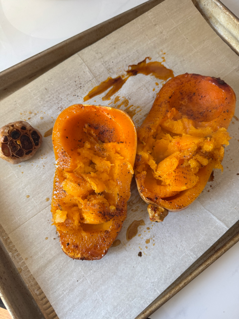 Roasted butternut squash halves and roasted garlic on a sheet pan