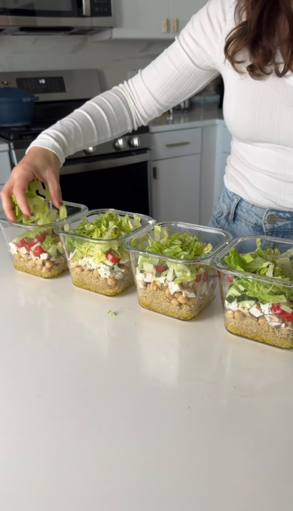 Adding shredded lettuce on top of layered salad containers