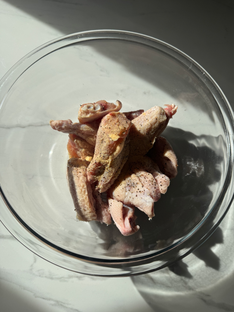 Chicken wings seasoned with garlic powder, salt, and pepper in a bowl