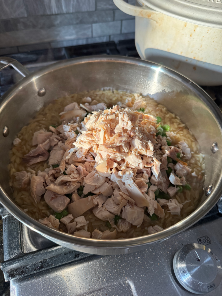 Shredded rotisserie chicken added to orzo in a skillet