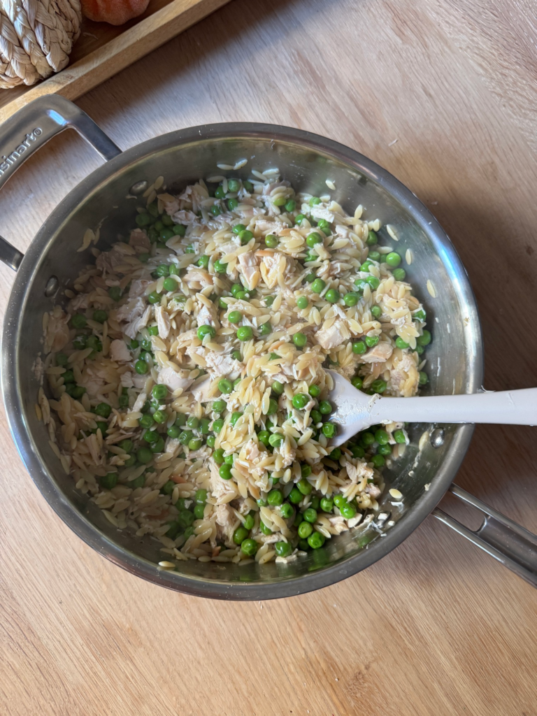 Creamy orzo with peas and shredded chicken in a skillet