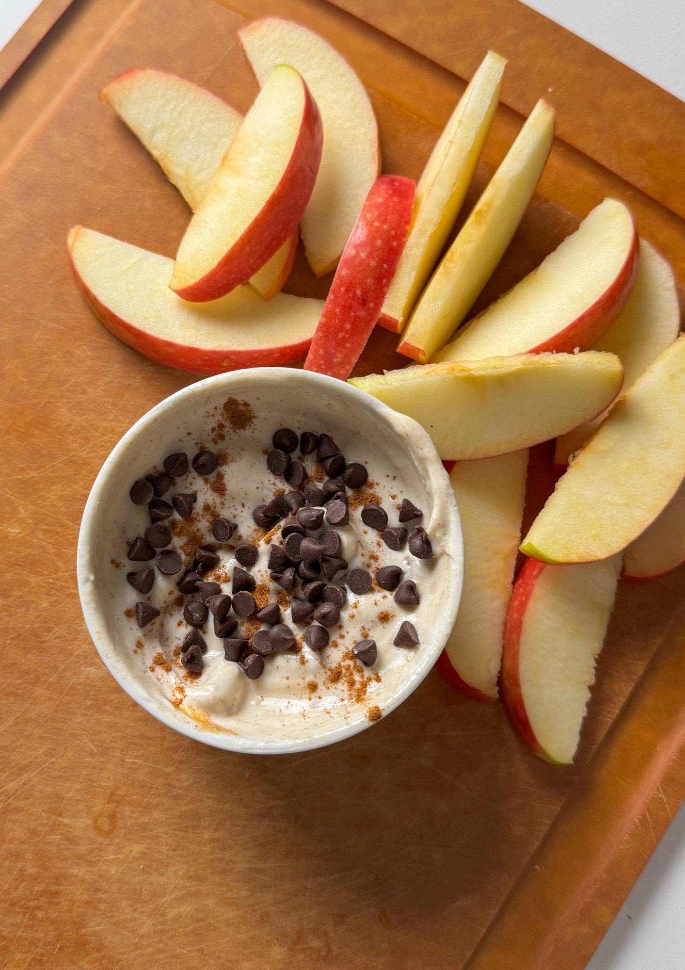 Protein apple dip topped with mini chocolate chips and cinnamon with apple slices