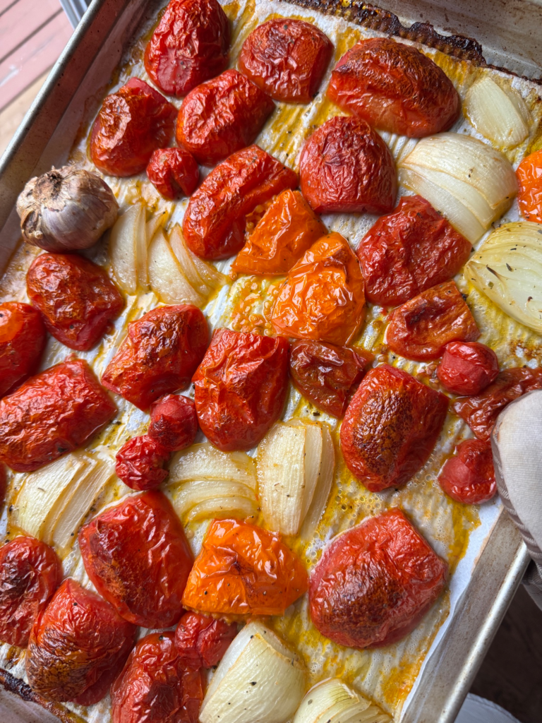Roasted Roma tomatoes, onion, and garlic on a baking sheet