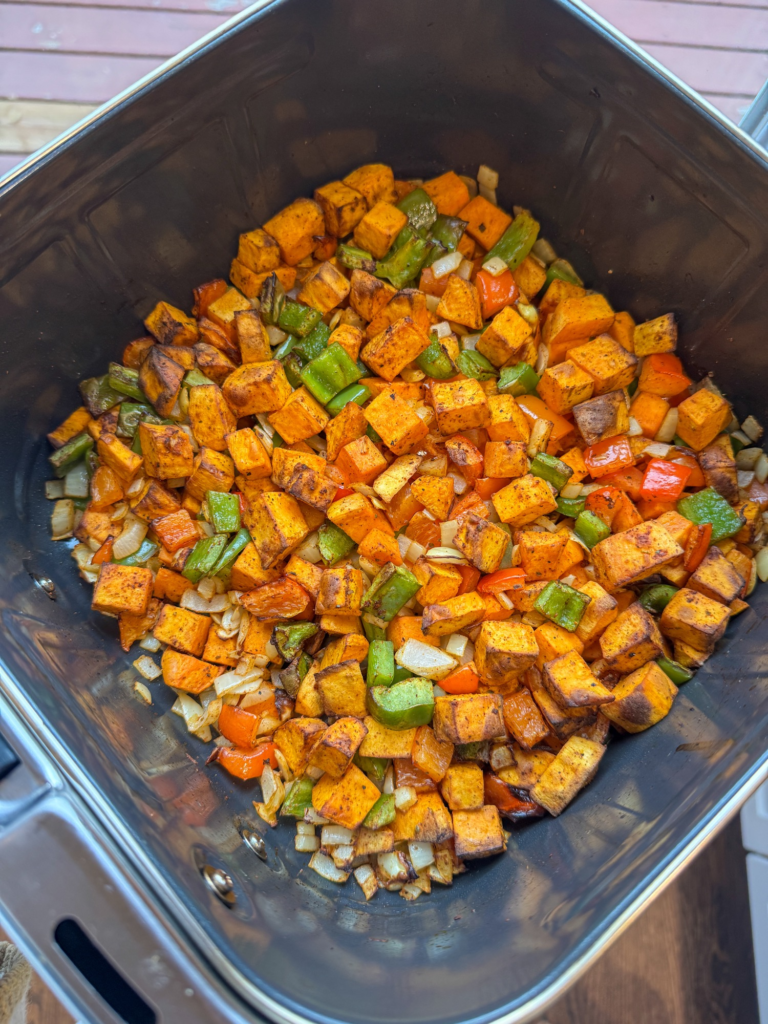Roasted sweet potatoes, bell peppers, and onions in an air fryer basket