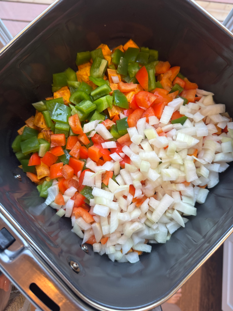 Diced peppers and onion added to sweet potatoes in an air fryer basket