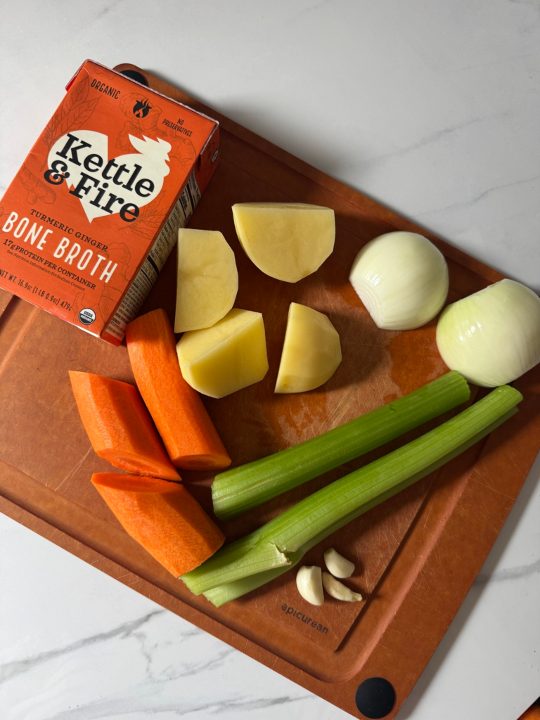 Ingredients for easy blended vegetable soup on a cutting board: carrot, celery, onion, potato, and broth