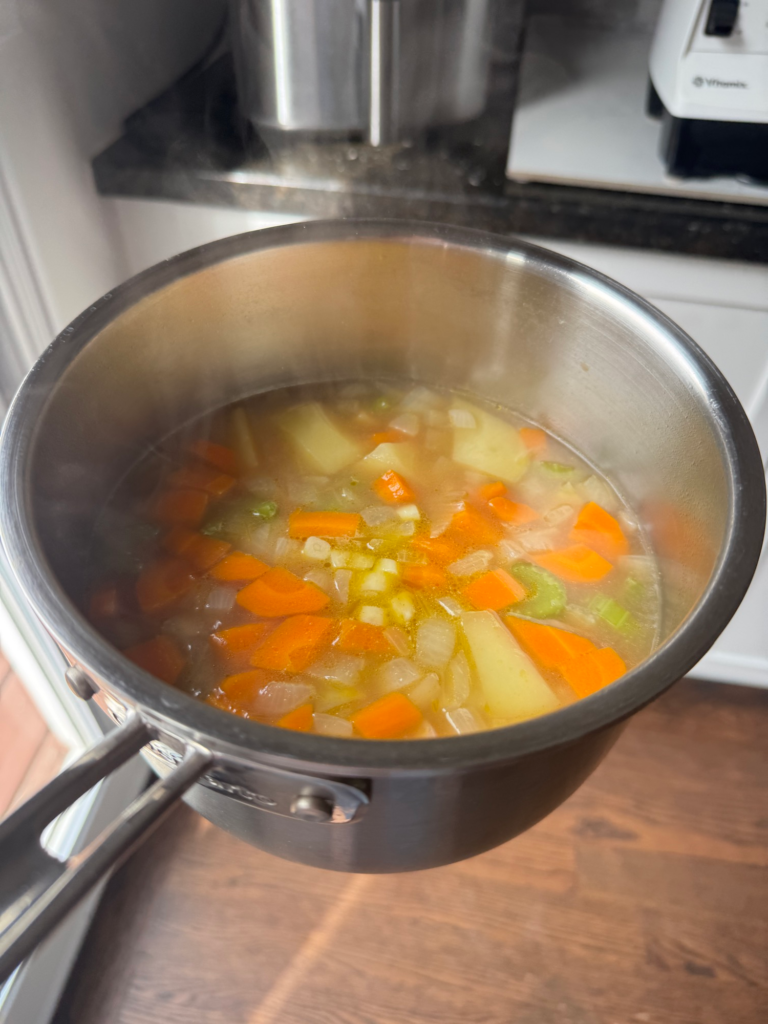 Vegetable soup simmering in a pot before blending, with carrots, celery, and potato