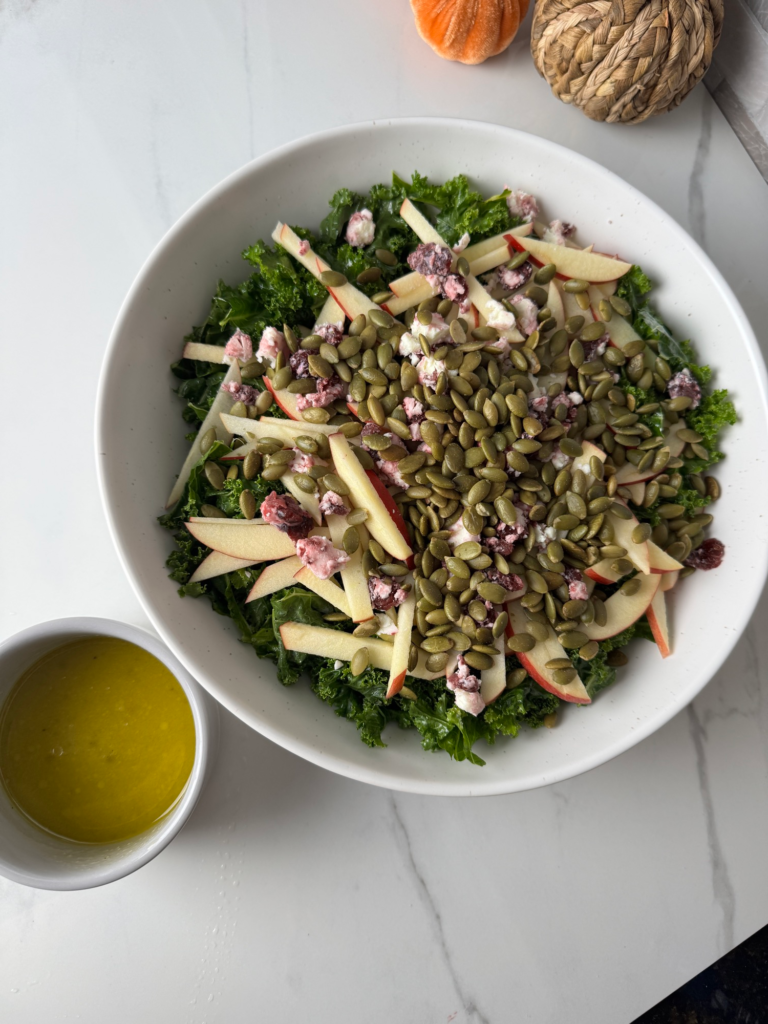Dressed kale salad topped with pepitas, apple, and goat cheese with dressing on the side