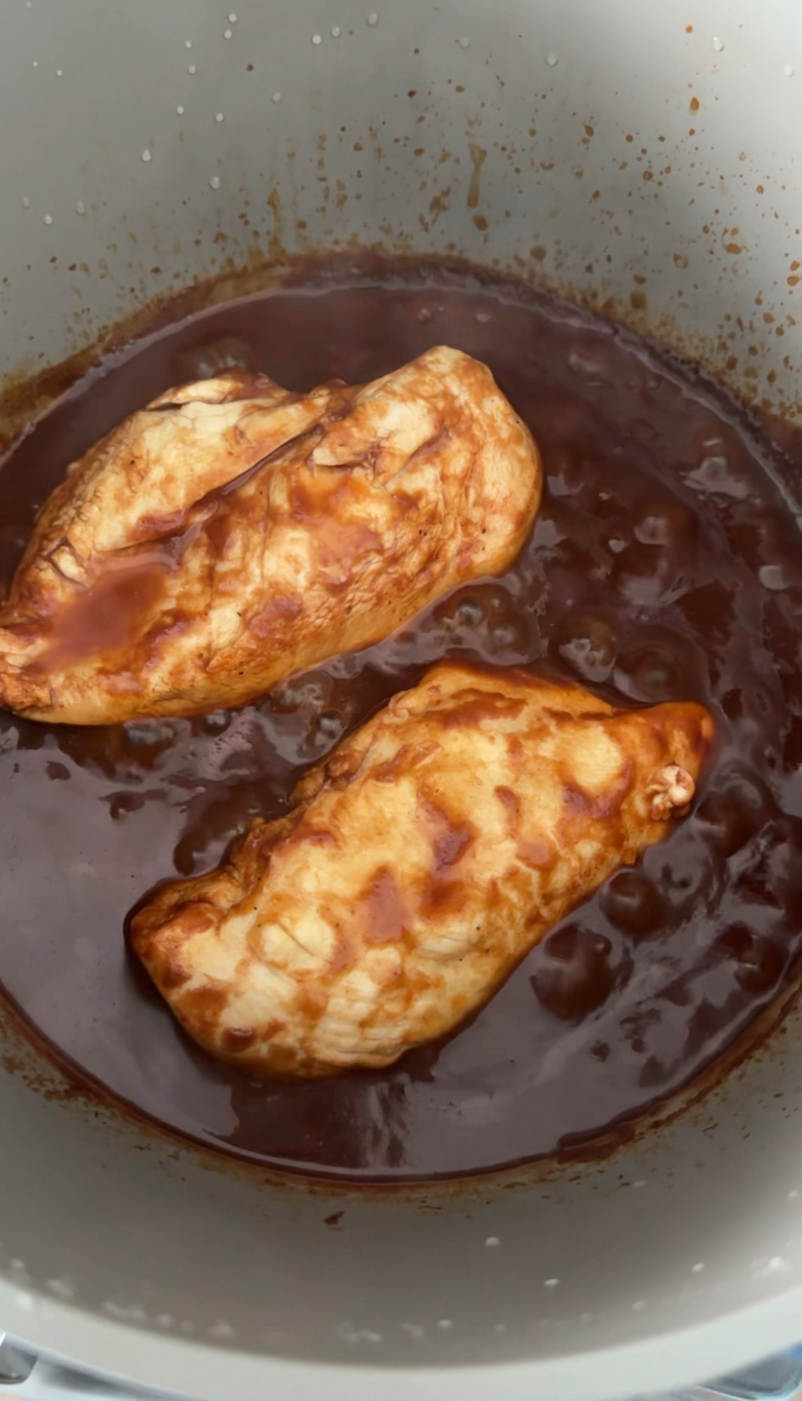 Chicken breasts simmering in barbecue sauce in a pot
