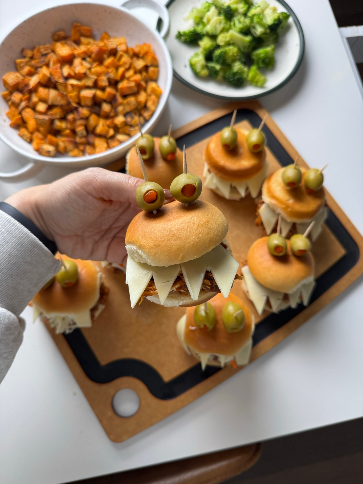 Hand holding a spooky BBQ chicken slider with provolone monster teeth and olive eyes
