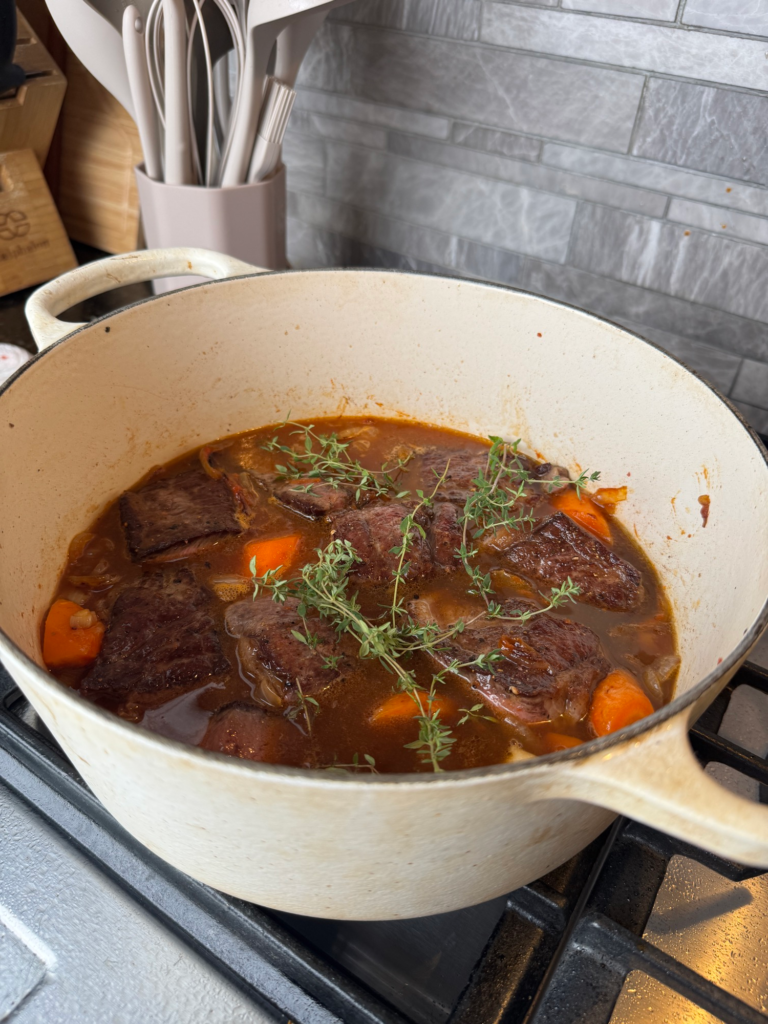 Beef ribs braising in apple cider with thyme in a Dutch oven