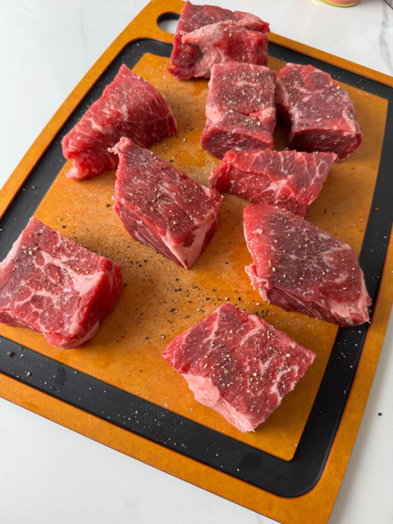 Raw boneless beef ribs seasoned with salt and pepper on a cutting board