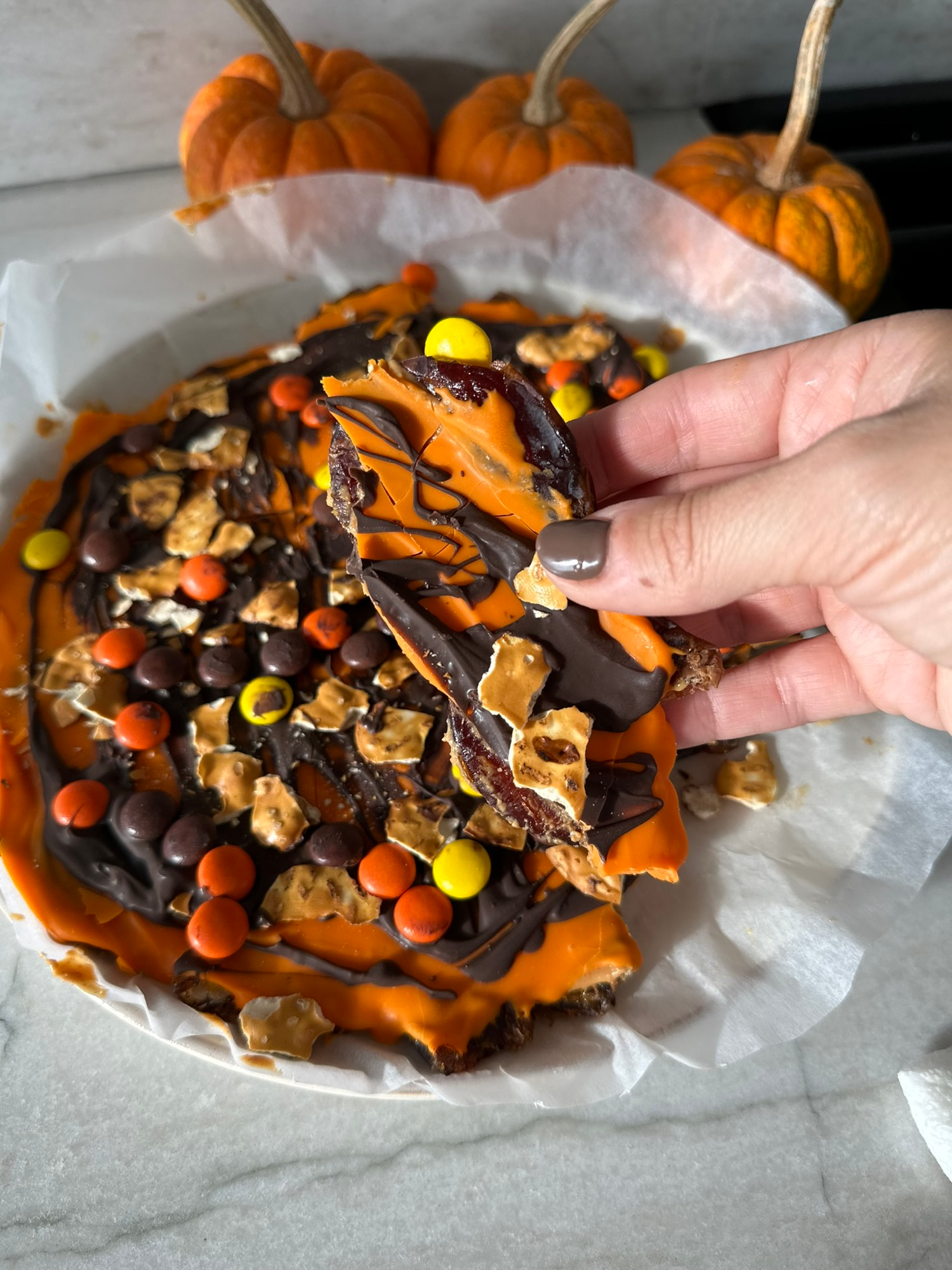 A hand breaking a piece of chocolate peanut butter date bark
