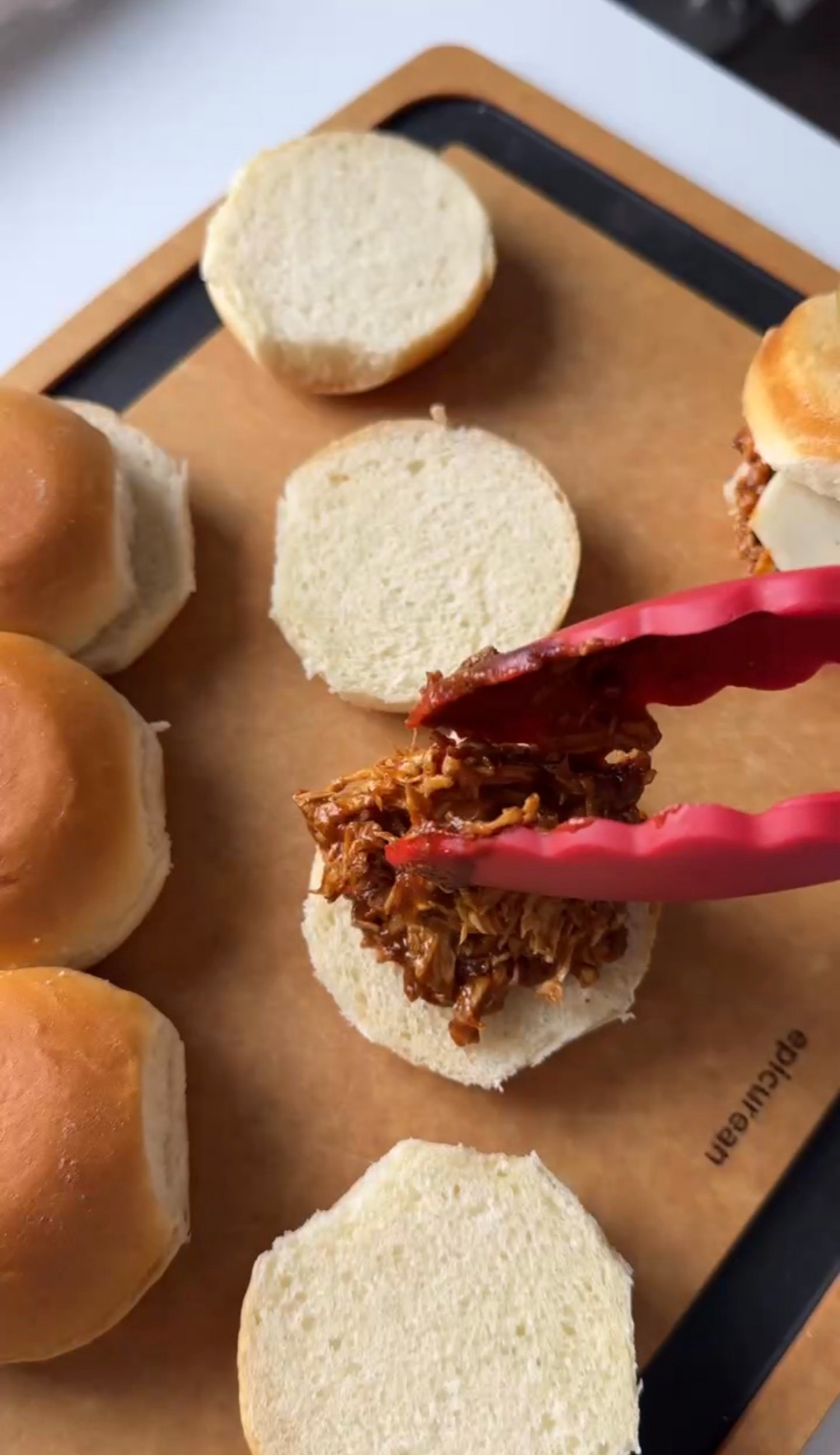 BBQ chicken being piled onto slider rolls
