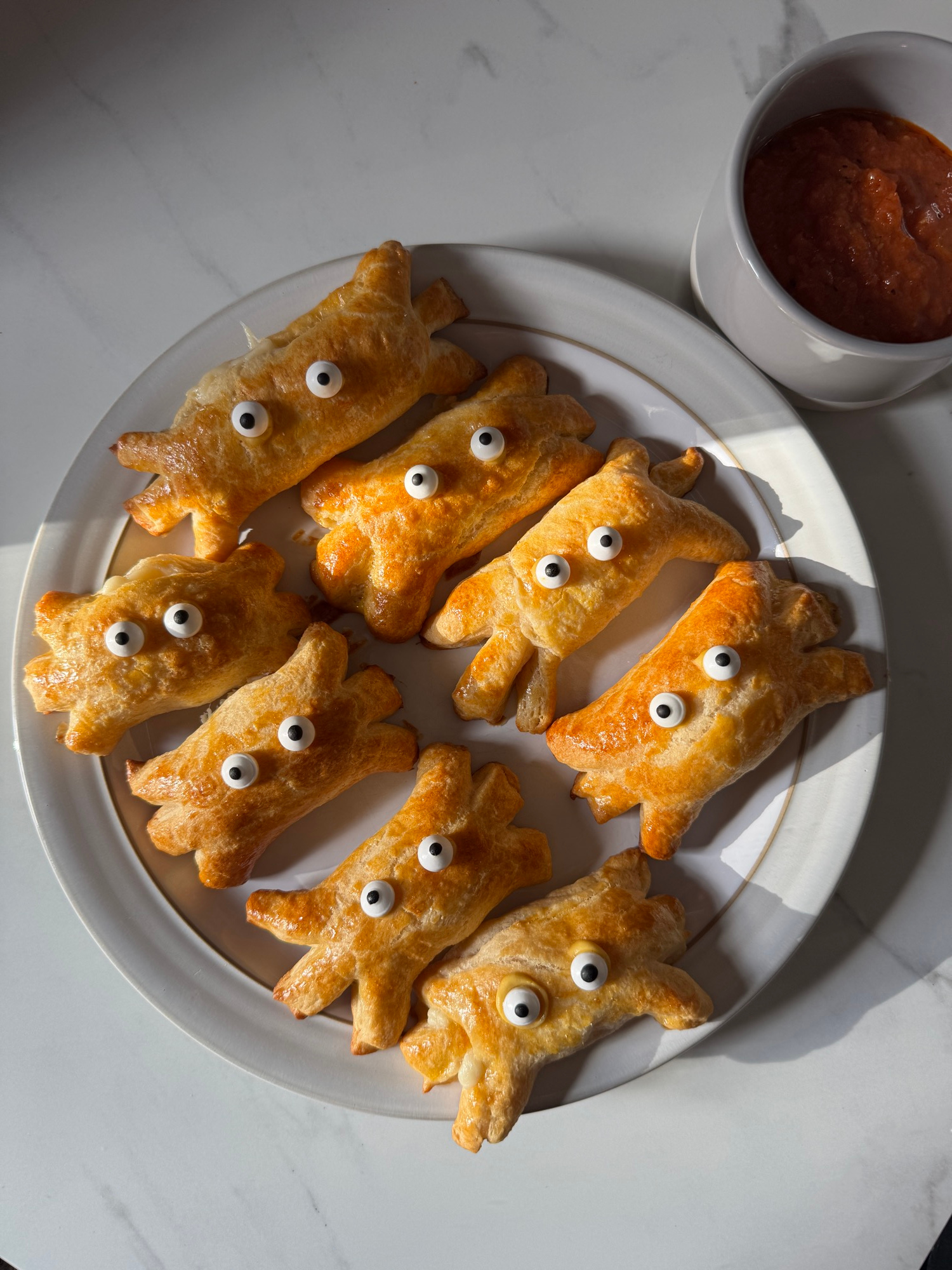 Crescent roll mozzarella spiders with candy eyes on a plate with marinara for dipping
