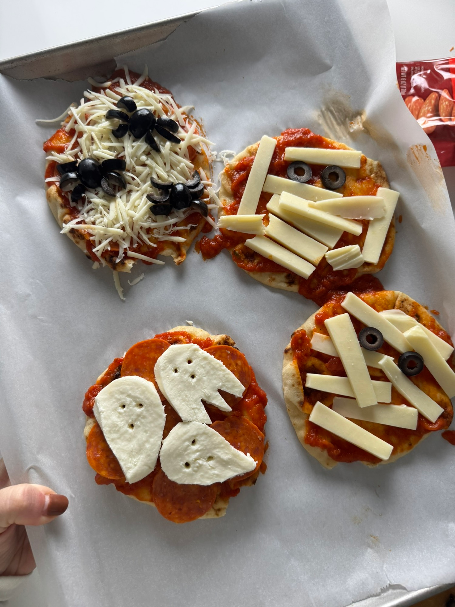 Naan pizzas decorated with cheese and olives as mummies, ghosts, and spiders before baking