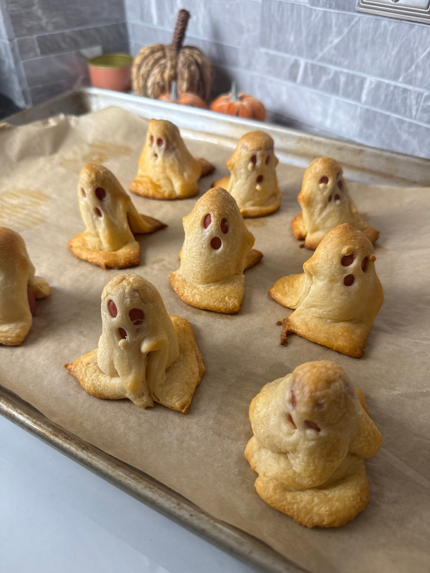 Golden baked ghost dogs made from hot dogs in crescent dough with ghost faces
