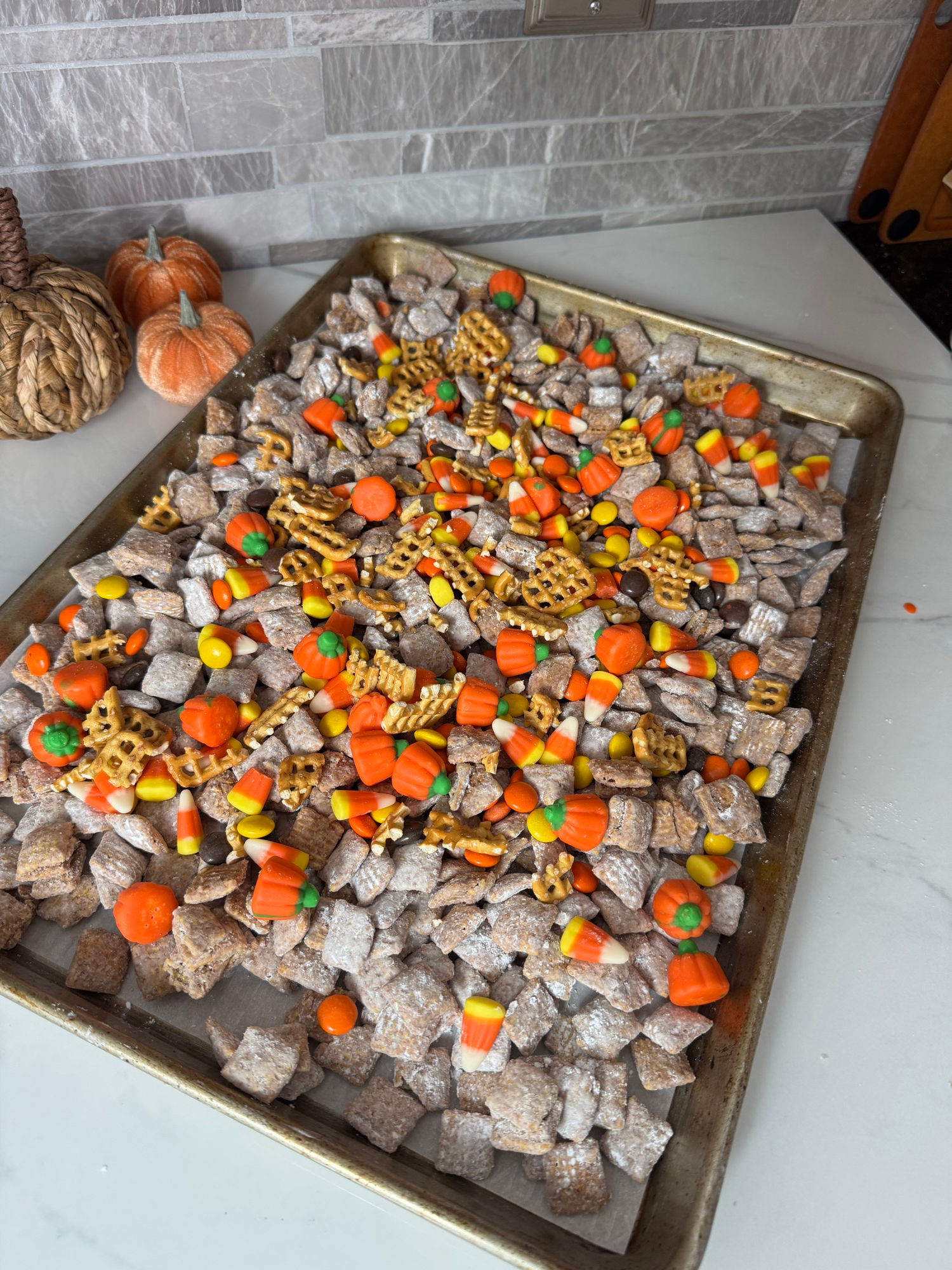 Halloween puppy chow on a baking sheet with candy corn, pumpkins, and pretzels
