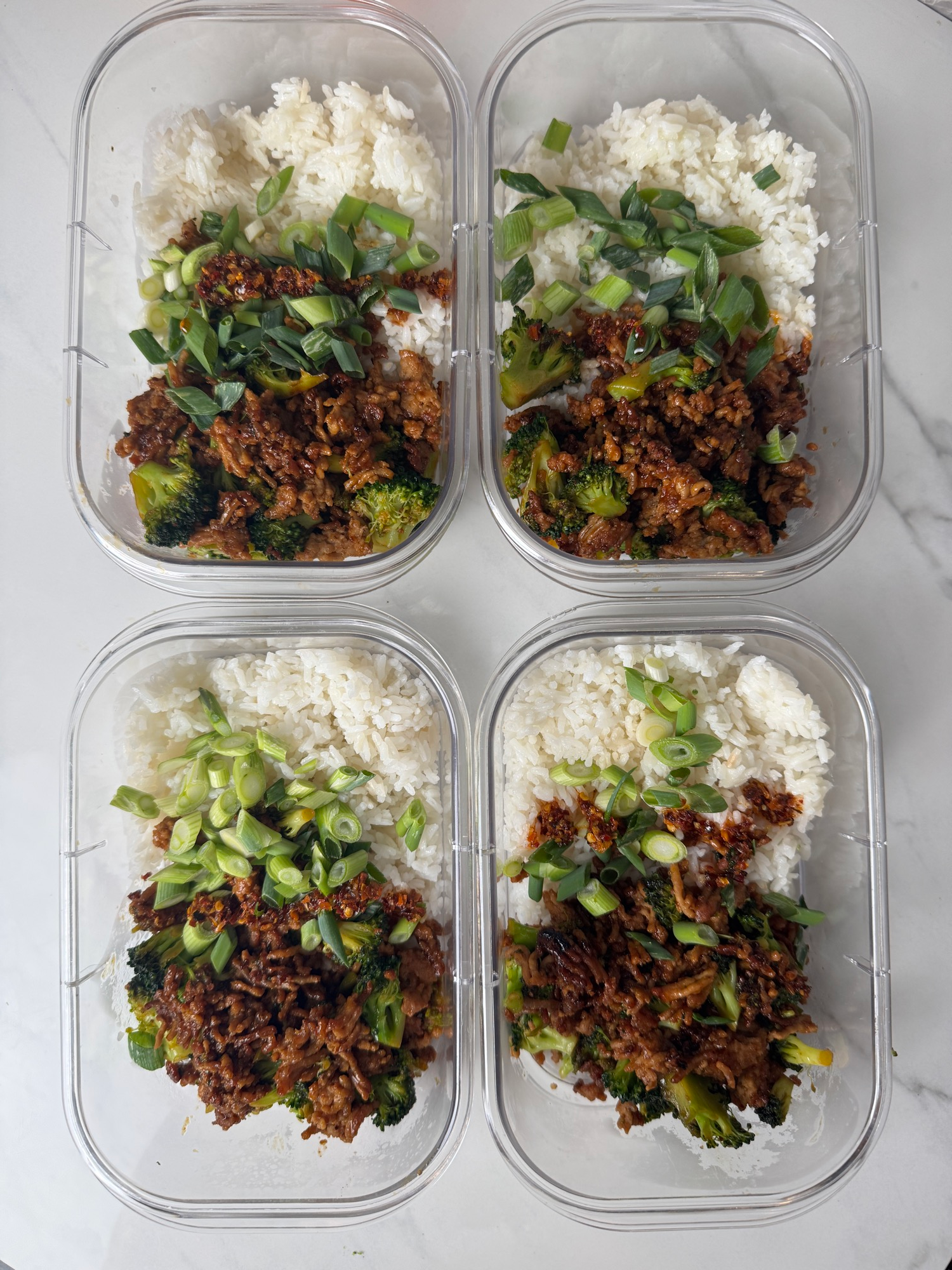Four meal prep containers of Korean ground pork rice bowls with broccoli and green onions