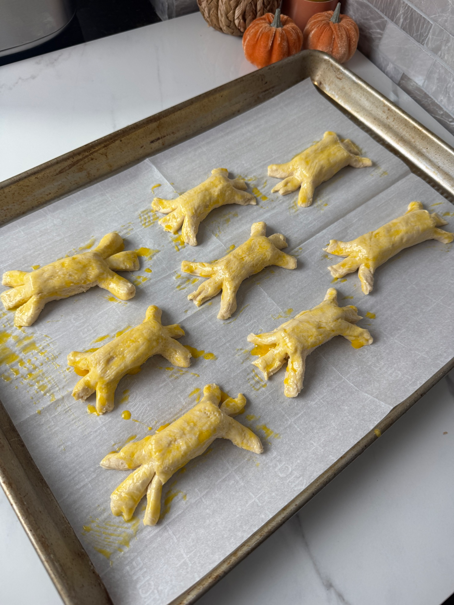 Raw mozzarella spiders brushed with egg wash on a baking sheet