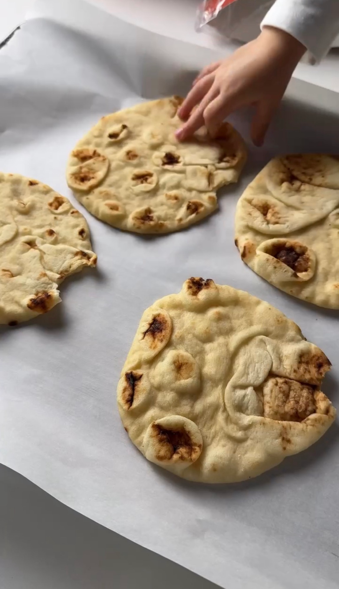 Plain naan breads on a parchment lined baking sheet