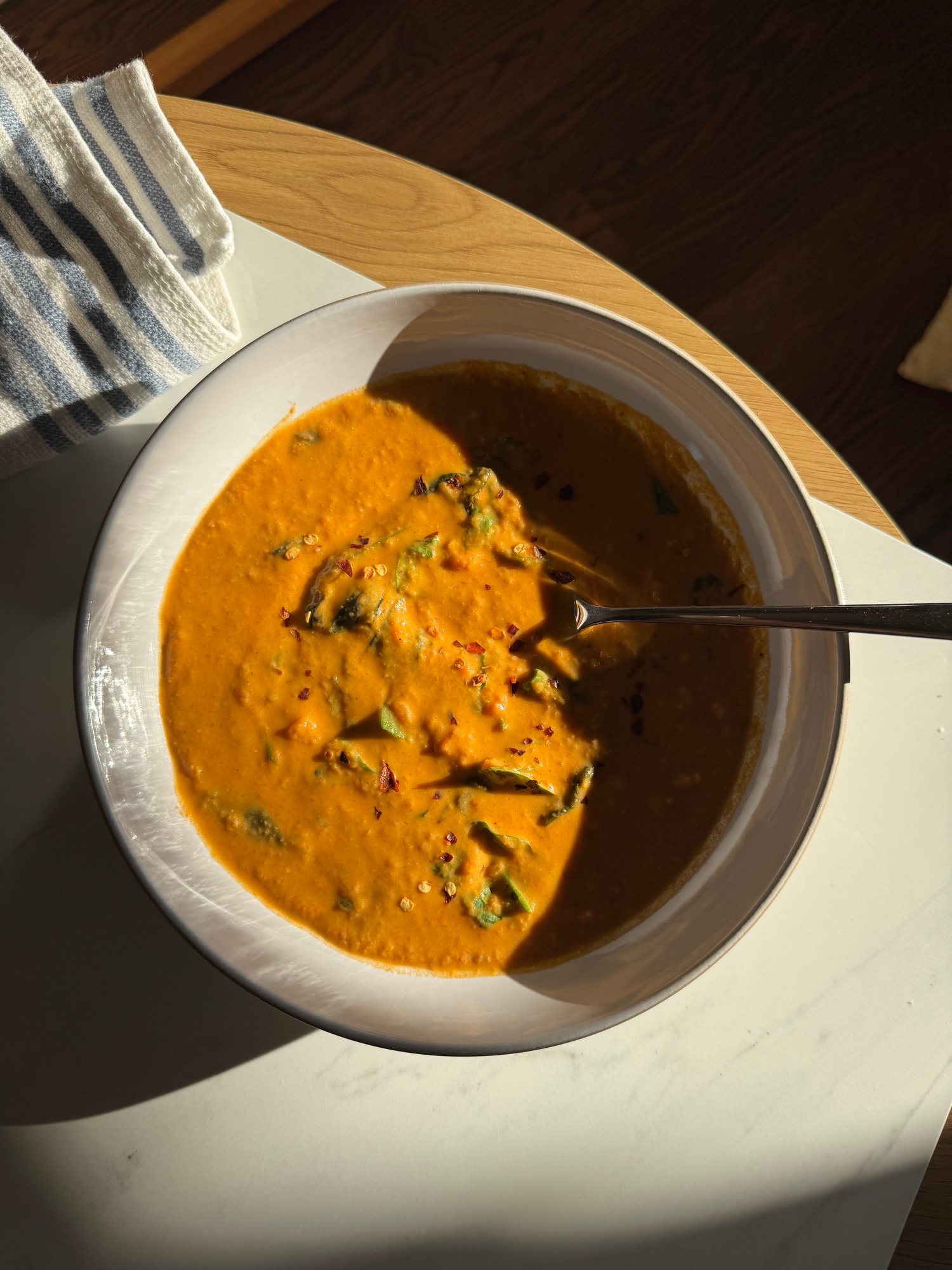 A bowl of creamy spiced lentil soup topped with spinach and chili flakes