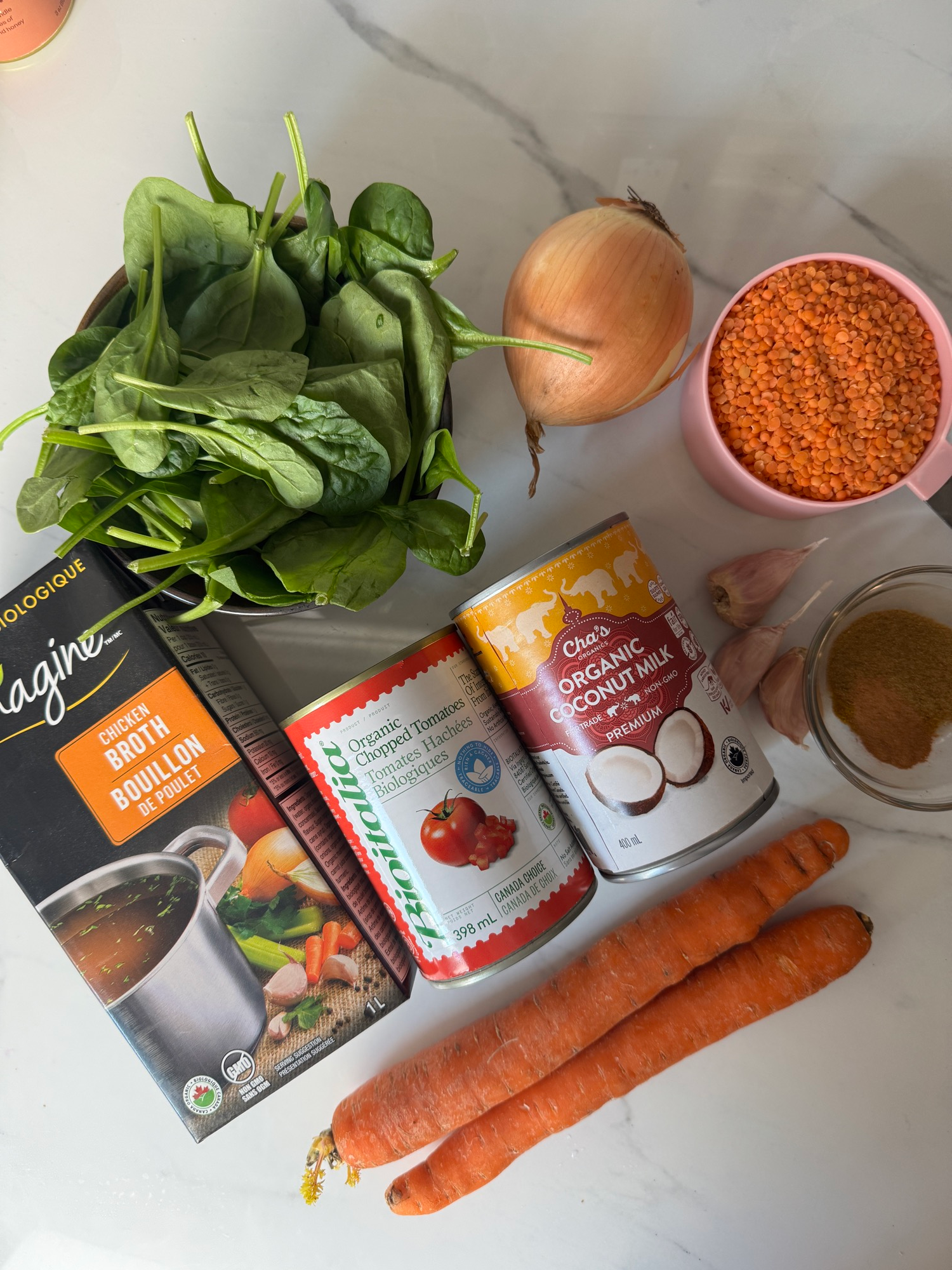 Ingredients for spiced lentil soup including red lentils, spices, coconut milk, tomatoes, carrots, and spinach