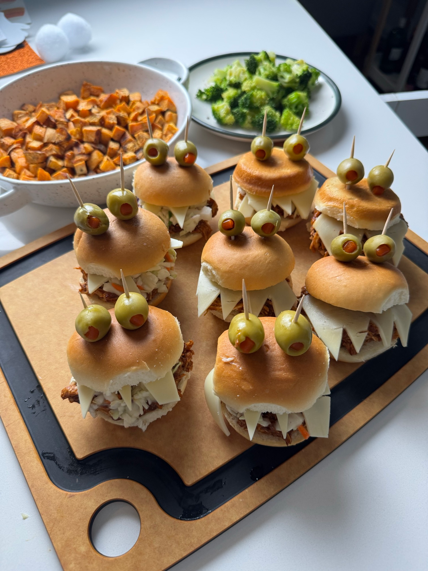 Platter of spooky BBQ chicken sliders with monster teeth and olive eyes, with roasted sweet potato and broccoli
