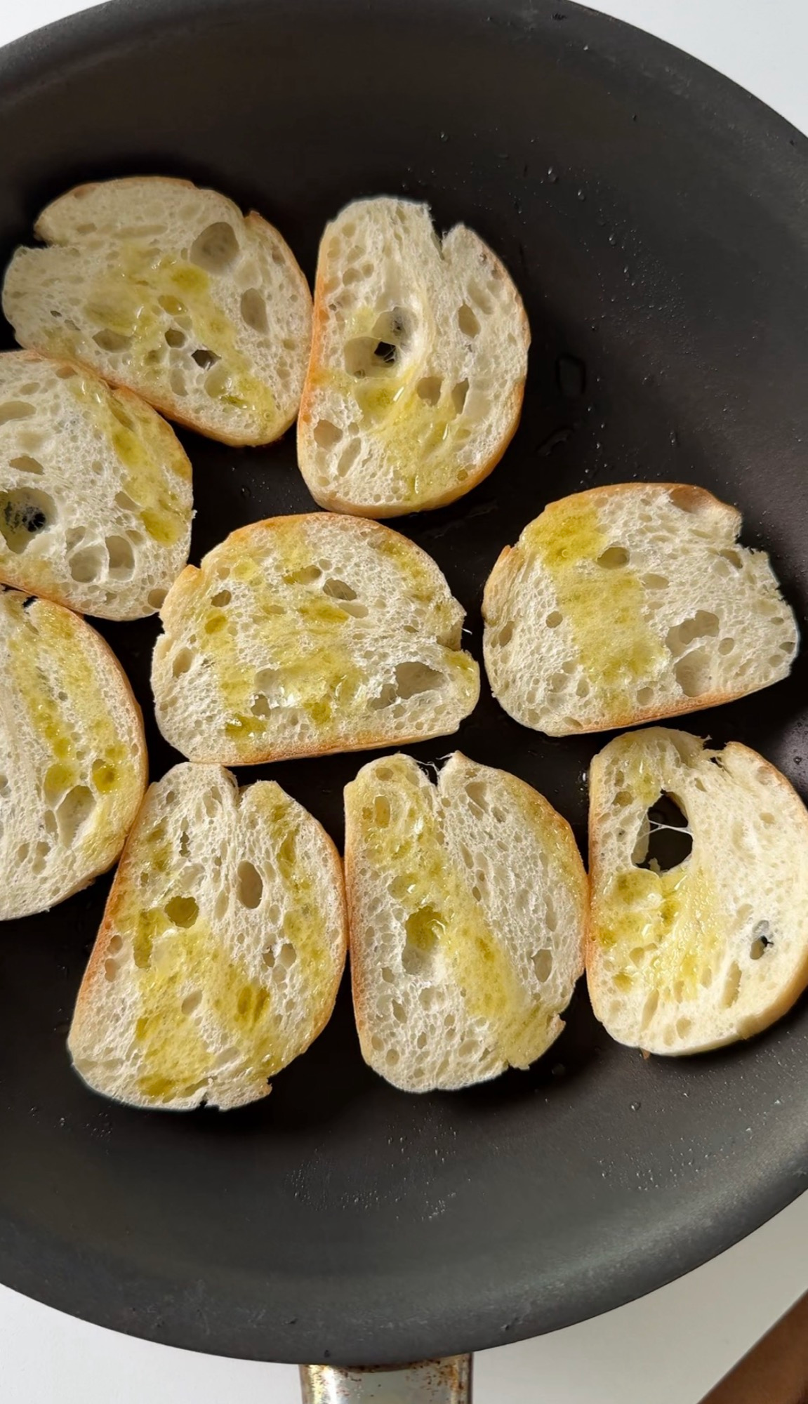 Baguette slices toasting in olive oil in a skillet